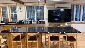 A modern kitchen with a large island, wooden chairs, and a built-in oven.