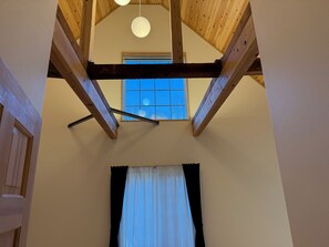 A room with a sloped ceiling, wooden beams, a window with a view, and a curtain. - Piccolo Mondo - Beautiful 7 bedroom lodge in lovely Yamanakako - BBQ/Onsen Bath (Minamitsuru District)