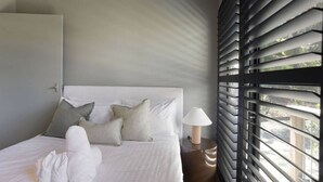 Un lit bien fait, avec des oreillers et des serviettes, une lampe de chevet et une fenêtre avec des stores.