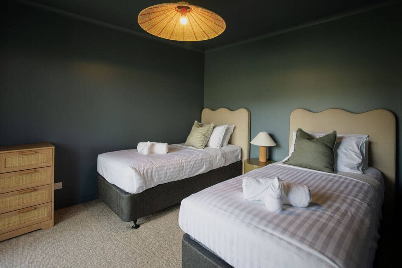 A bedroom with two beds, a wooden dresser, and a hanging light fixture.