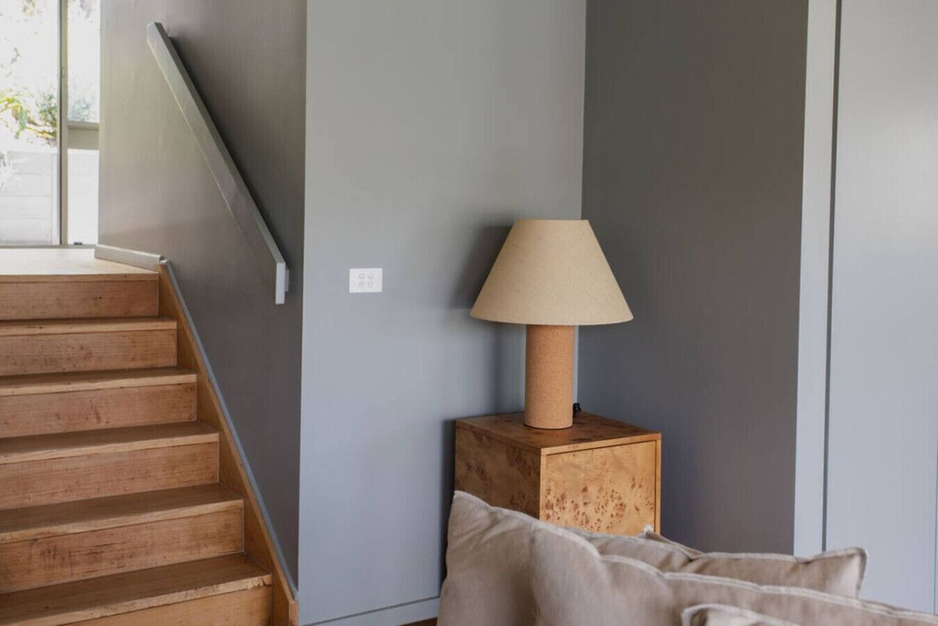 A staircase leading to a landing with a wooden finish, a beige lamp on a wooden nightstand, and a grey wall.