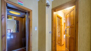 A hotel hallway with a wooden door and a glass elevator door. - Casa D`Amato - Roccaraso (Roccaraso)