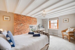 Une chambre avec un mur en briques, un lit avec une literie blanche, une commode, une chaise et une fenêtre donnant sur un paysage agréable.