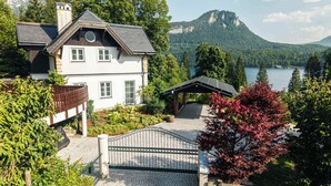 A two-story house with a balcony, a covered patio, and a view of a lake and mountains. - Villa Victoria | Sauna | Parking | Garden (Fischerndorf)