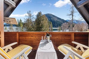 Una terraza de madera con una mesa dispuesta para dos, con vistas a un paisaje montañoso.
