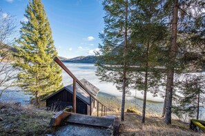 Une cabane dotée d’une terrasse en bois et offrant une vue sur un lac entouré d’arbres.