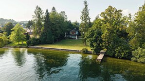 Een vakantiehuis aan het meer met een steiger, een gazon en een modern huis omringd door bomen.