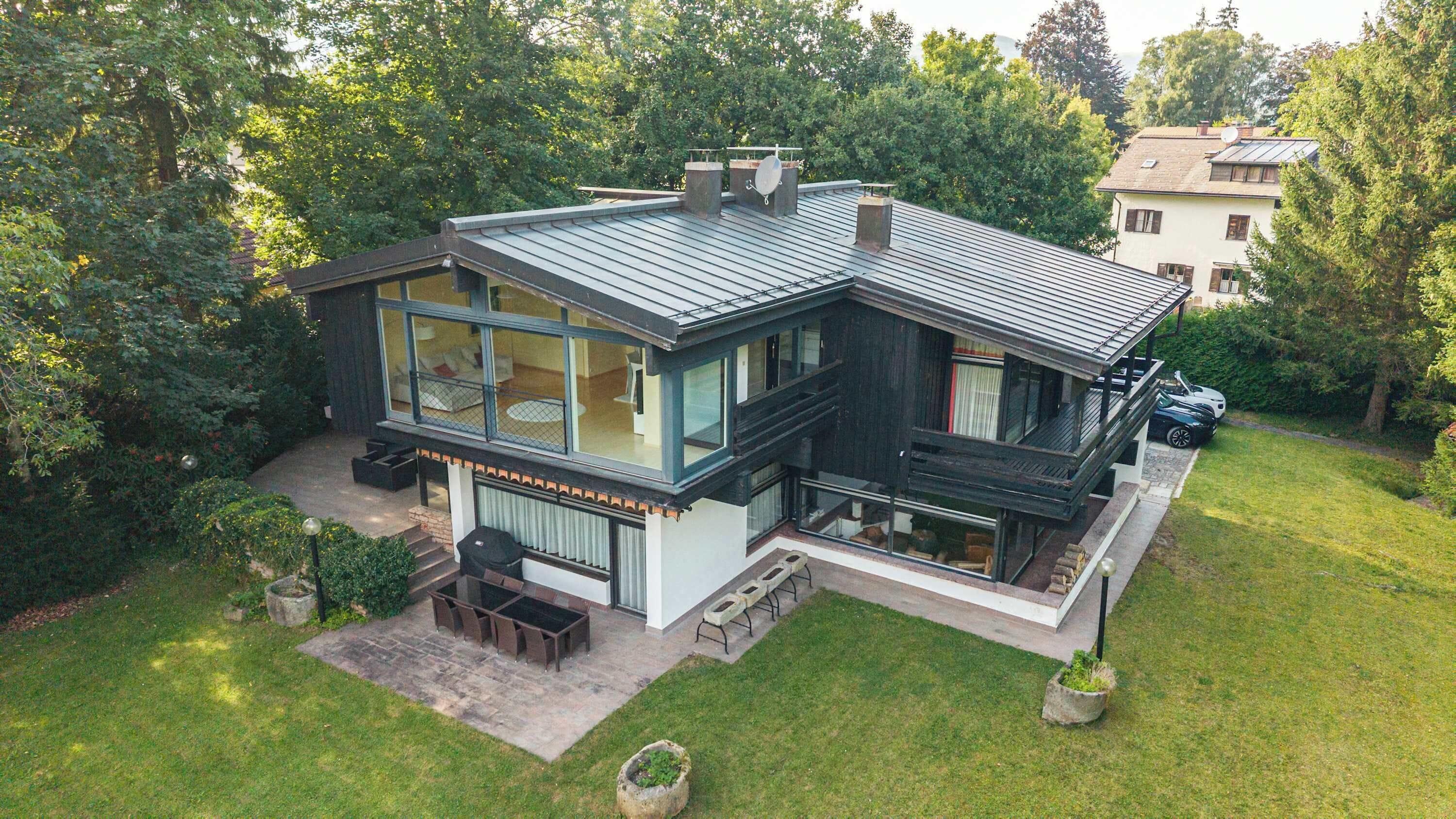 A modern two-story house with large windows, a covered patio, and a car parked in the driveway.