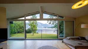 Een moderne slaapkamer met een grote schuifdeur naar een balkon met uitzicht op een meer en bergen.