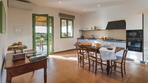 A modern kitchen with a dining area, featuring a wooden table and chairs, a built-in oven, and a large window with a view. - Beautiful brand new villa with pool - DiCasaInSicilia (Menfi)