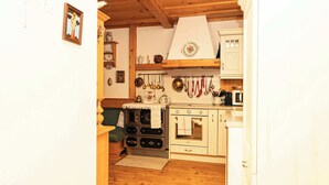 A compact kitchen with wooden cabinets, a stove, and hanging utensils. - Apartment Narzisse | Lakefront | Kitchen | Parking (Gößl)