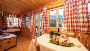 A cozy wooden cabin with plaid curtains, a dining table set with food and wine, and large windows offering mountain views. - Apartment Narzisse | Lakefront | Kitchen | Parking (Gößl)