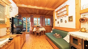 A cozy cabin interior with a wooden dining area, a green sofa, and a television. - Apartment Narzisse | Lakefront | Kitchen | Parking (Gößl)