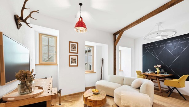 Un salon moderne avec une table basse en bois, un canapé blanc, une suspension rouge et un tableau noir orné de dessins géométriques.