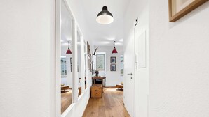Un couloir doté d’un plancher en bois, de murs blancs et d’une table centrale sur laquelle est posé un vase.