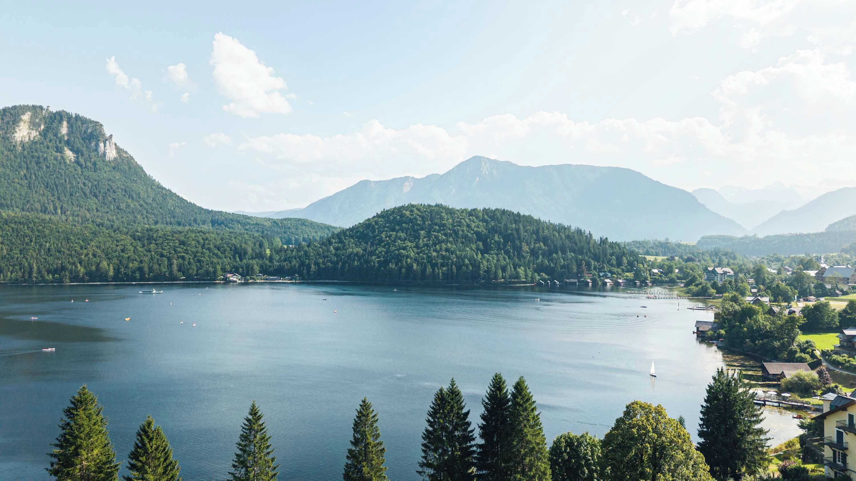A lake surrounded by forested mountains, with a small town in the foreground.