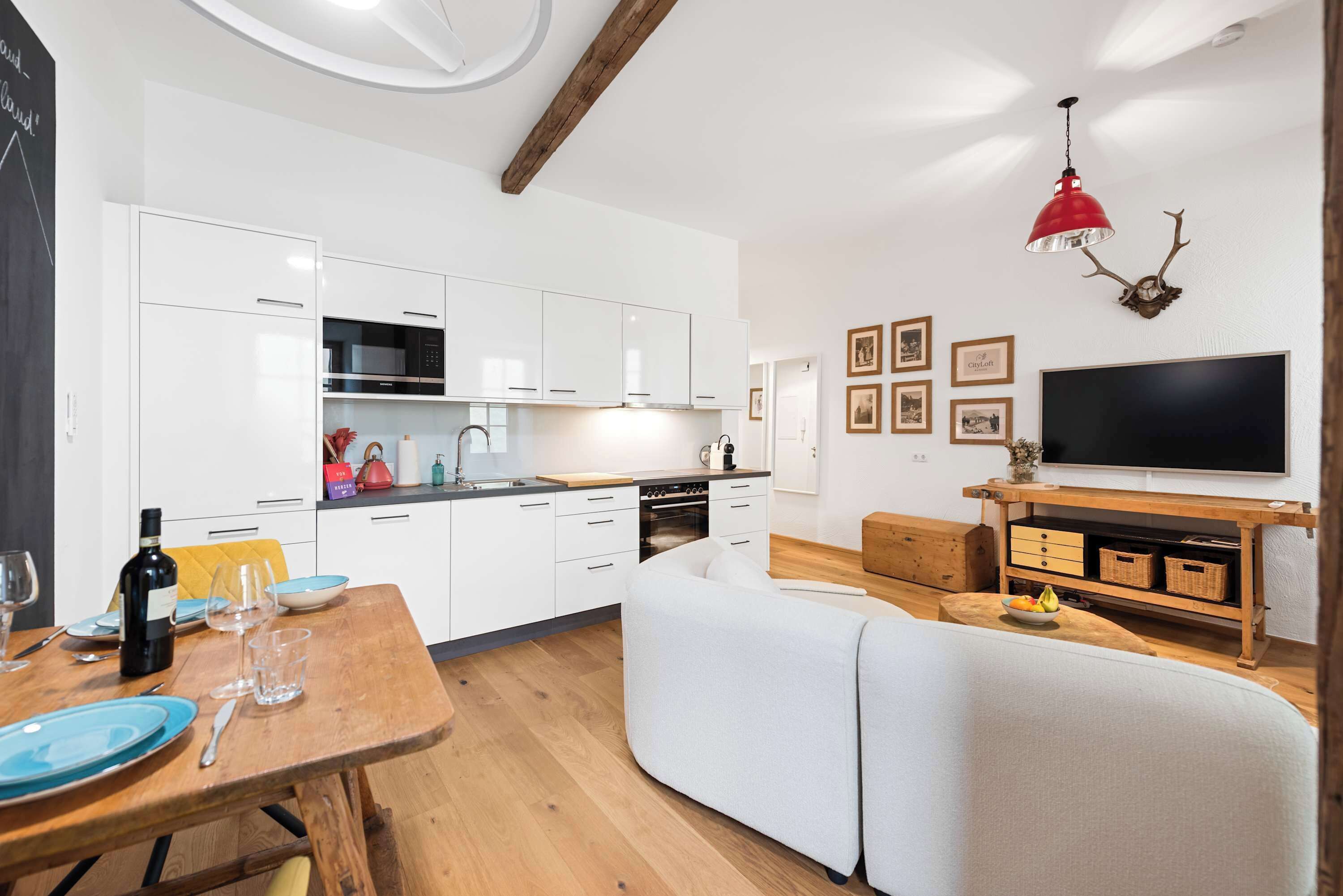 Una cucina moderna con mobili bianchi, un tavolo da pranzo in legno e una lampada a sospensione rossa.