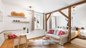 A cozy living room with a sofa, a coffee table, and a wooden bench. There are shelves with decorative items and a window with curtains. - Superior Studio | Kitchen | Parking | Central (Bad Aussee)