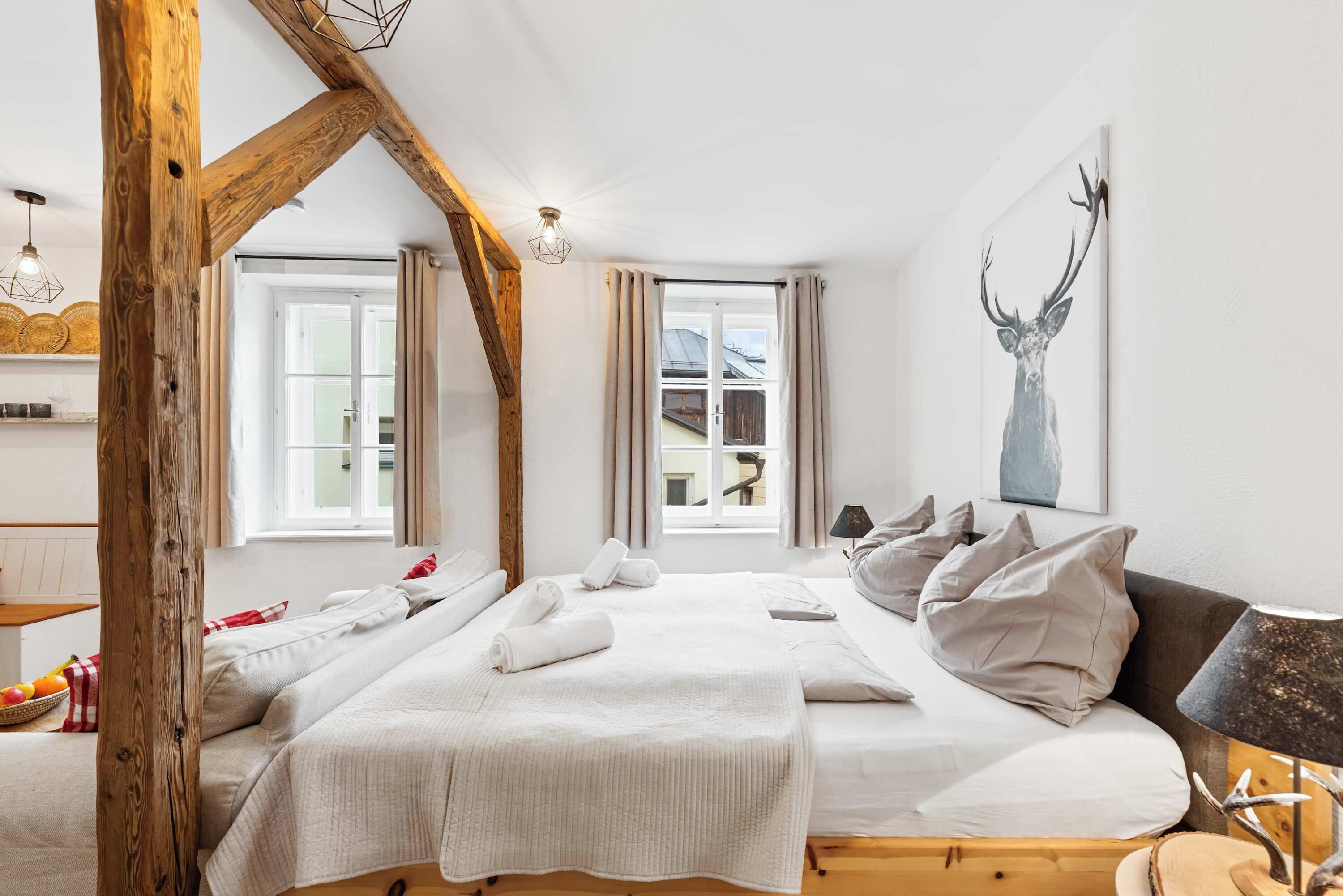 Une chambre avec un grand lit, une poutre en bois au plafond et une fenêtre avec des rideaux.