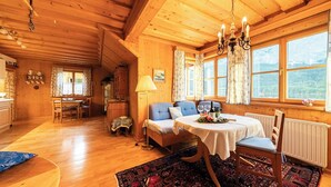 L’intérieur d’un chalet en bois chaleureux et accueillant, avec un coin repas, deux fauteuils bleus à revêtement en tissu, une table recouverte d’une nappe blanche et un lustre.