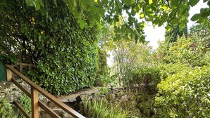 Eine Steintreppe mit Holzgeländer, die zu einem Gartenbereich mit verschiedenen Pflanzen und einem kleinen Wasserspiel führt.