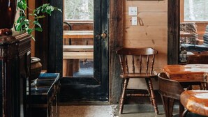A rustic wooden interior with a wooden door, a table, chairs, a lamp, and a framed picture on the wall.