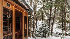 A wooden cabin with a large glass door, surrounded by snow-covered trees.