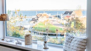 Ett fönster med utsikt över en kuststad, en lampa, en kudde och en liten prydnadssak på fönsterbrädan.
