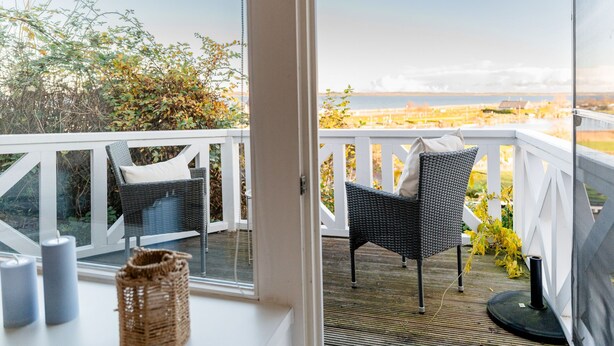 En balkong med flätade stolar och utsikt över havet.