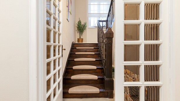A staircase with wooden steps and a handrail, leading to a landing with a window and a potted plant. - Holiday Home 'Pension Seeblick' with Lake View, Private Garden and Wi-Fi (Holzappel)