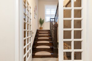 Una scala in legno con corrimano, che porta a un pianerottolo con una finestra e una pianta in vaso.