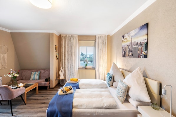 A cozy room with a sofa, a bed with pillows, a small table with a vase, and a window with curtains.