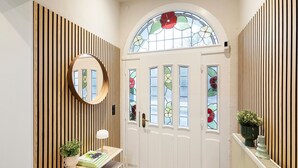 A hallway with a white door, a round mirror, a wooden slat wall, and a small table with a plant and a book. - Holiday Home 'Pension Seeblick' with Lake View, Private Garden and Wi-Fi (Holzappel)
