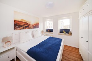 Ein Schlafzimmer mit einem Bett, einem Nachttisch, einer Lampe, einem Fenster mit Ausblick und einem Bild an der Wand.
