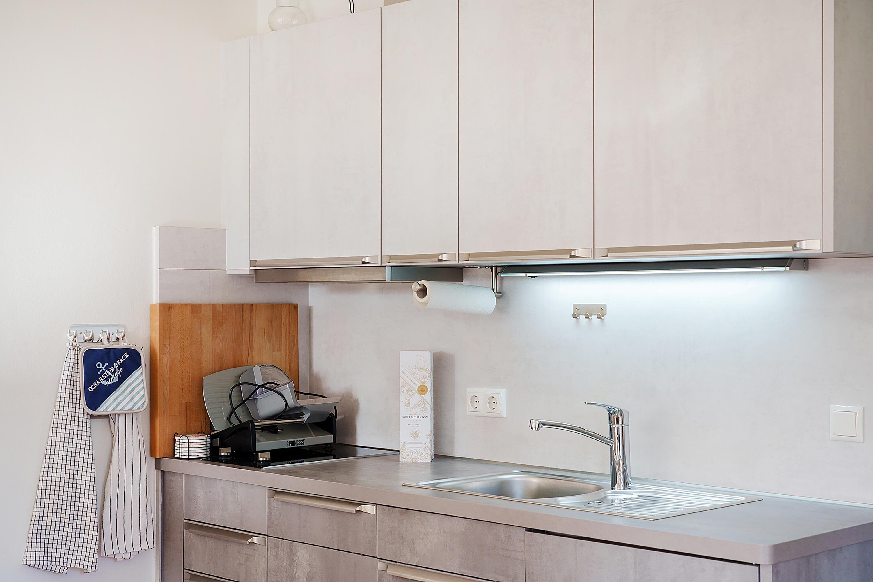 A modern kitchen with a stainless steel sink, a microwave, and a toaster. There are cabinets above the counter and a towel rack with a towel hanging on it.