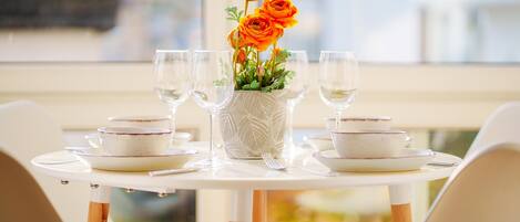 A dining table set with white plates, bowls, and glasses, centered with a vase of orange flowers.