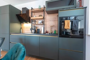 Une cuisine moderne dotée d’appareils électroménagers intégrés, d’étagères en bois et d’une fenêtre donnant sur l’intérieur.