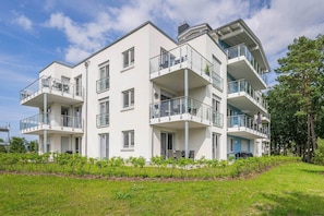 Un immeuble résidentiel à plusieurs étages, doté de balcons, d’une pelouse devant et surplombant un ciel dégagé.