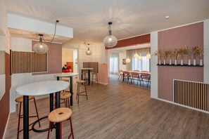 Un espace repas moderne avec une table ronde, des tabourets de bar, des luminaires suspendus et une étagère murale agrémentée d’objets décoratifs.