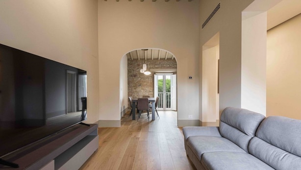 Ein modernes Wohnzimmer mit Flachbildfernseher, grauem Sofa, Holzboden und Steinwand.