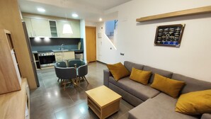 Een moderne woonkamer met een grijze bank, een glazen eettafel en een keuken op de achtergrond.