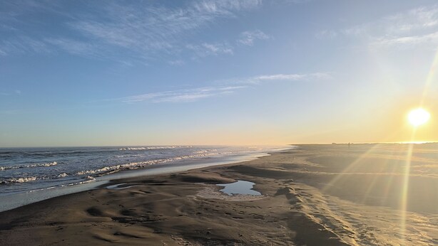 Een strand met een heldere lucht en de zon die aan de horizon ondergaat.
