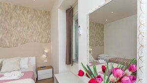 A hotel room with a bed, bedside table, mirror, and a vase with flowers. - Apartment 'Il Tulipano House' with Private Terrace, Wi-Fi and Air Conditioning (Catania)