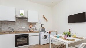 A modern kitchen with built-in appliances, a dining area with a table set for two, and a flat-screen TV mounted on the wall. - Apartment 'Il Tulipano House' with Private Terrace, Wi-Fi and Air Conditioning (Catania)