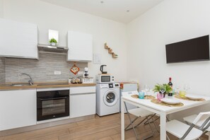 Una cocina moderna con electrodomésticos integrados, una zona de comedor con una mesa dispuesta para dos personas y un televisor de pantalla plana montado en la pared.