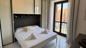 Una camera d'albergo moderna con un letto grande, una scrivania con un computer e vista sugli edifici attraverso la finestra.