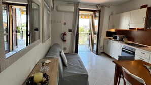 Un ambiente compatto con angolo cottura, divano e zona pranzo.