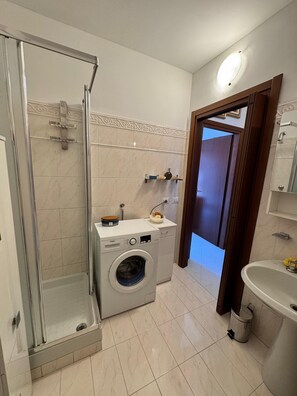A compact bathroom with a glass-enclosed shower, a built-in washing machine, and a sink. - Two Bedroom Apartment with Terrace 5 min from Metro - Direct to Duomo/Fiera + Free Wi-Fi (Sesto San Giovanni)