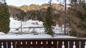 Paisaje nevado con una terraza de madera al frente, una montaña en el fondo y un edificio con techo inclinado.