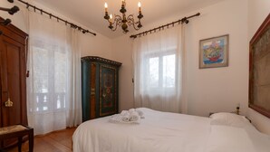 Un dormitorio con una cama grande, un armario de madera, una araña y un cuadro en la pared.